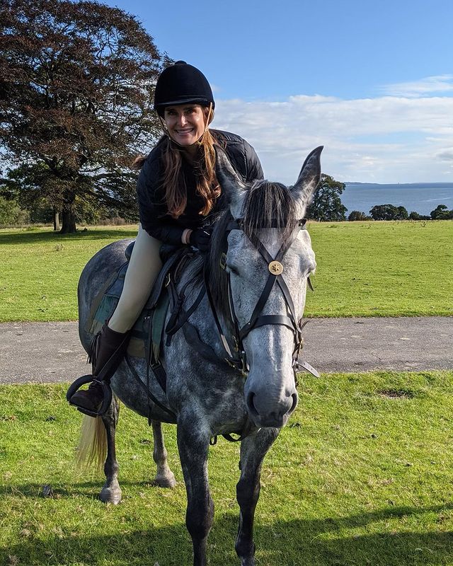 Brooke Shields riding a horse in a black jockey hat and white pants.